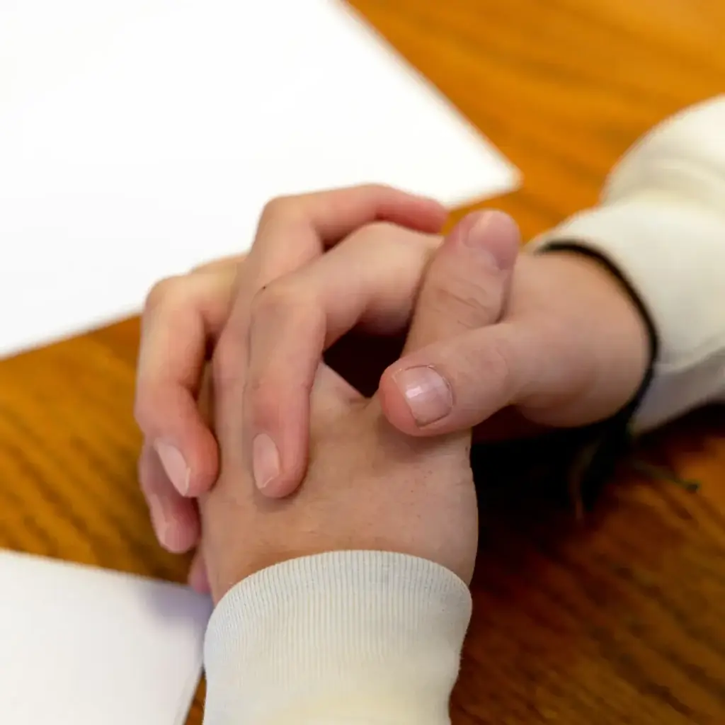 Close up of clasped hands on a wooden table.