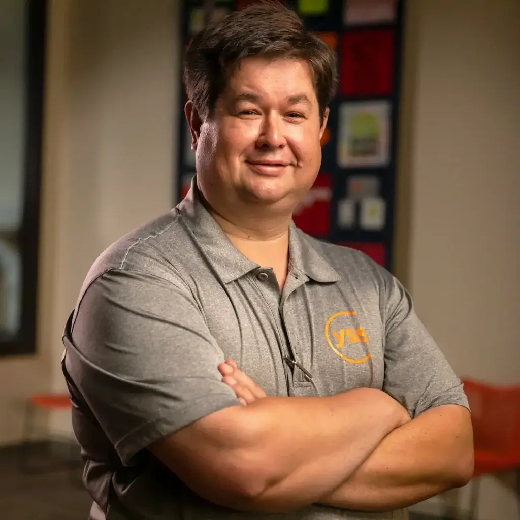 Man wearing a YSS shirt, smiling at camera with arms crossed.