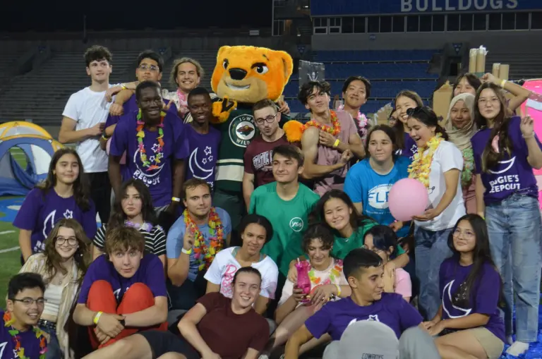 A large group of young adults pose together with a cat mascot.