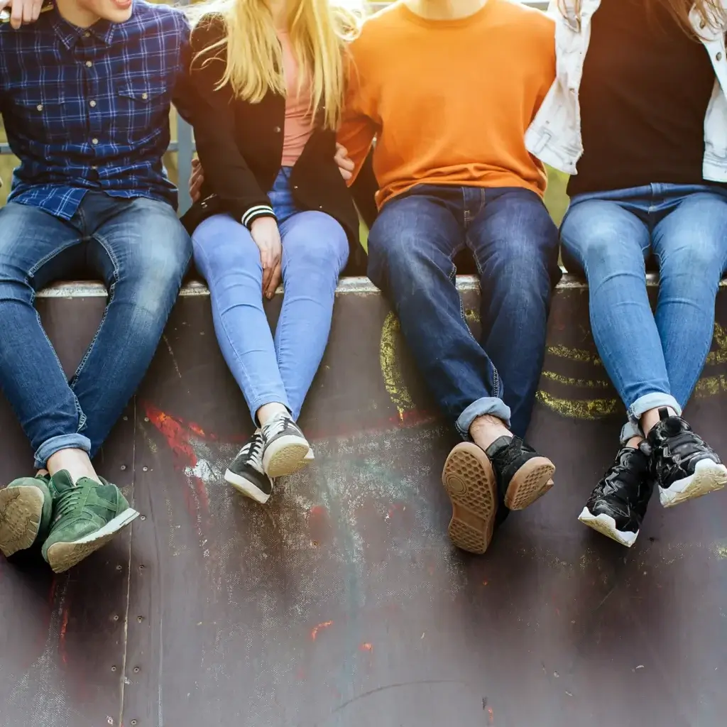 Four teens sitting in a row on a concrete wall, with their ankles crossed.