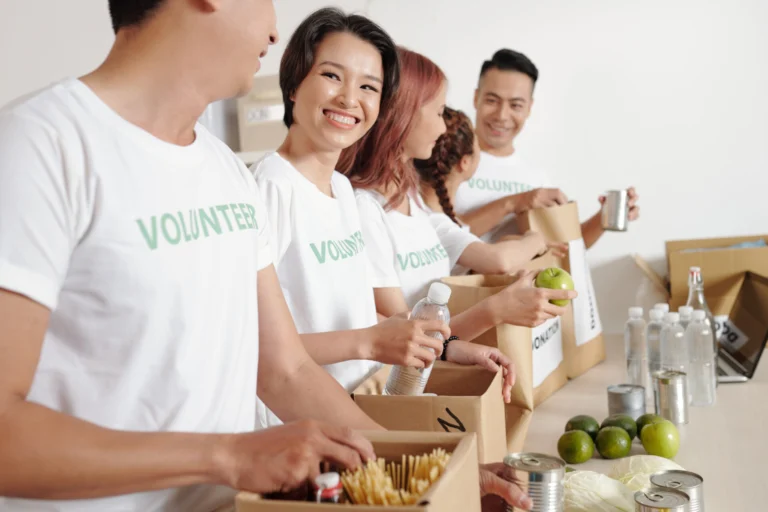 A woman smiles at a fellow volunteer while packing food in cardboard boxes.