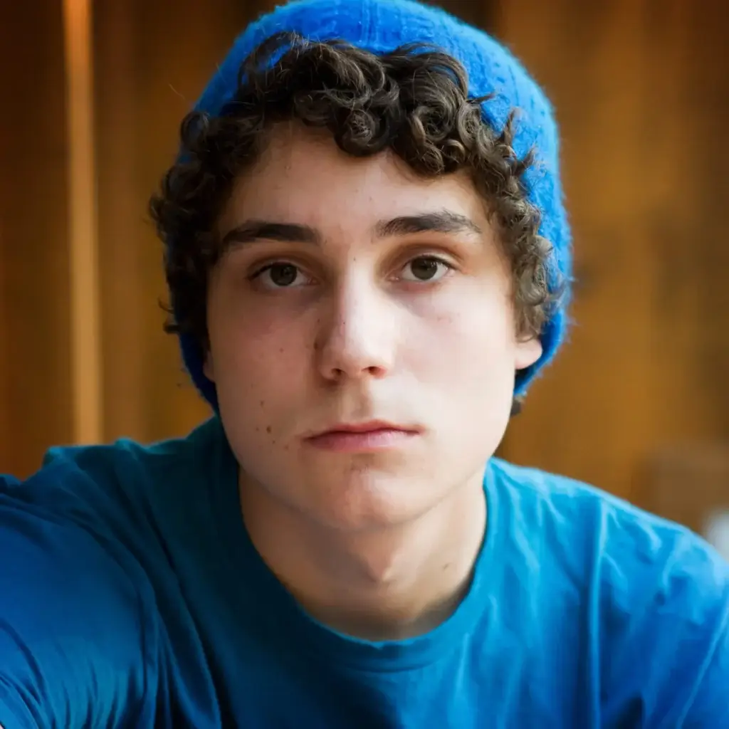 Teen boy wearing a blue shirt and blue beanie, looking at the camera with a neutral expression.