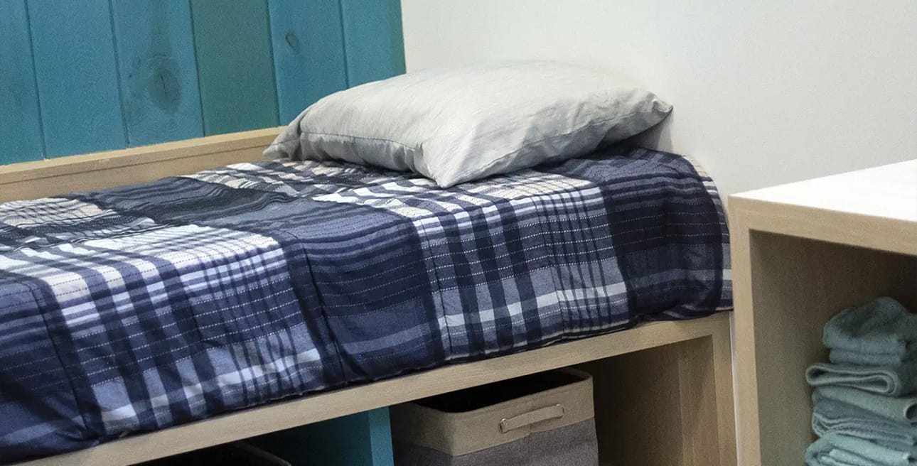 A twin bed with blue plaid sheets and storage bins underneath.