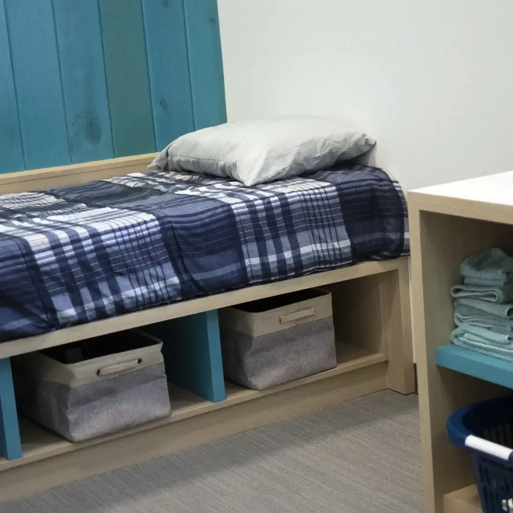 A twin bed with blue plaid sheets and storage bins underneath.
