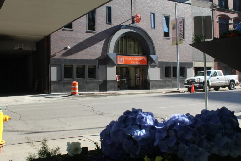 Exterior of a building with an arched entryway and an orange sign that says Youth Opportunity Center