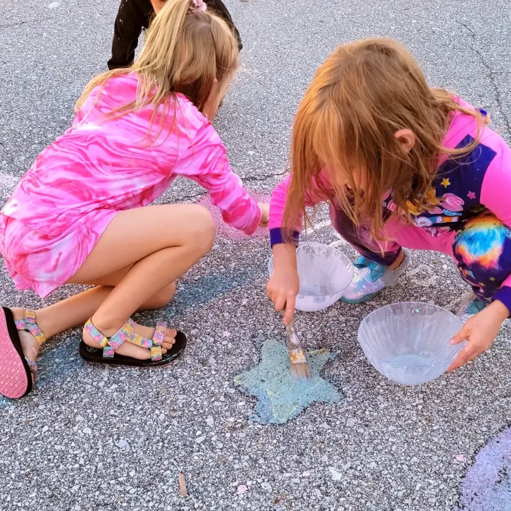 Two girls painting on the sidewalk with chalk and water.