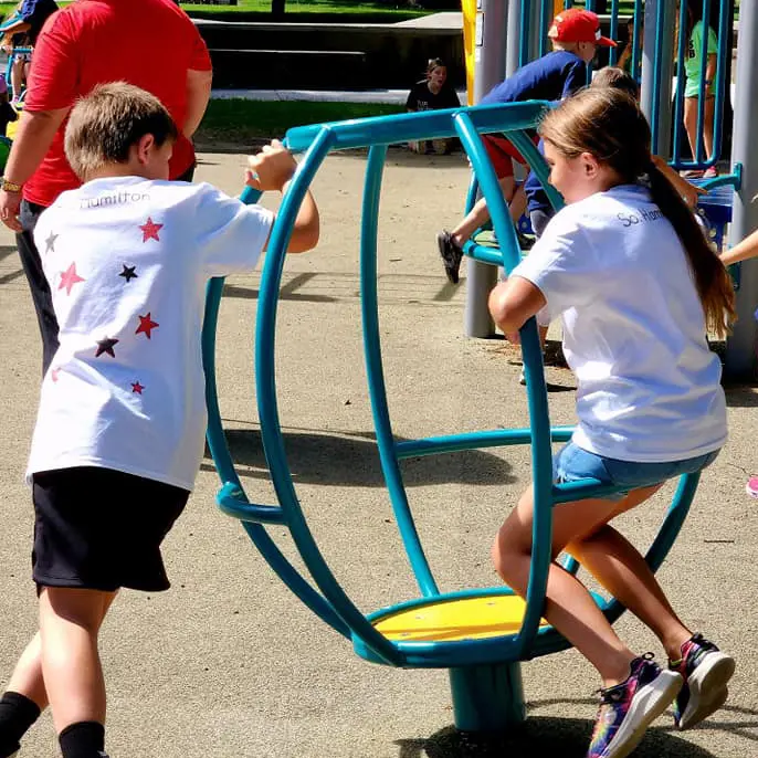 A boy and a girl play together at a playground on a sunny day.