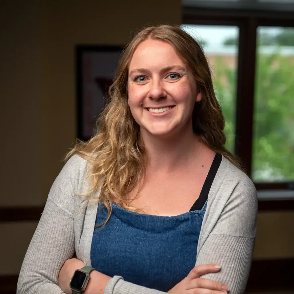 Woman with wavy hair smiling at camera with arms crossed.