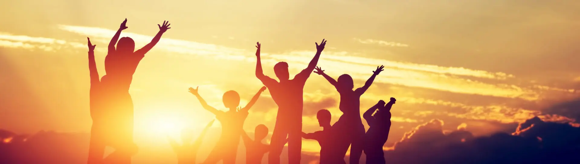 Silhouettes of happy adults and children raising their arms in front of a sunset