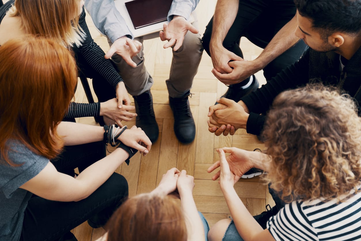 Close up of hands of teenagers sitting in a circle during a support meeting