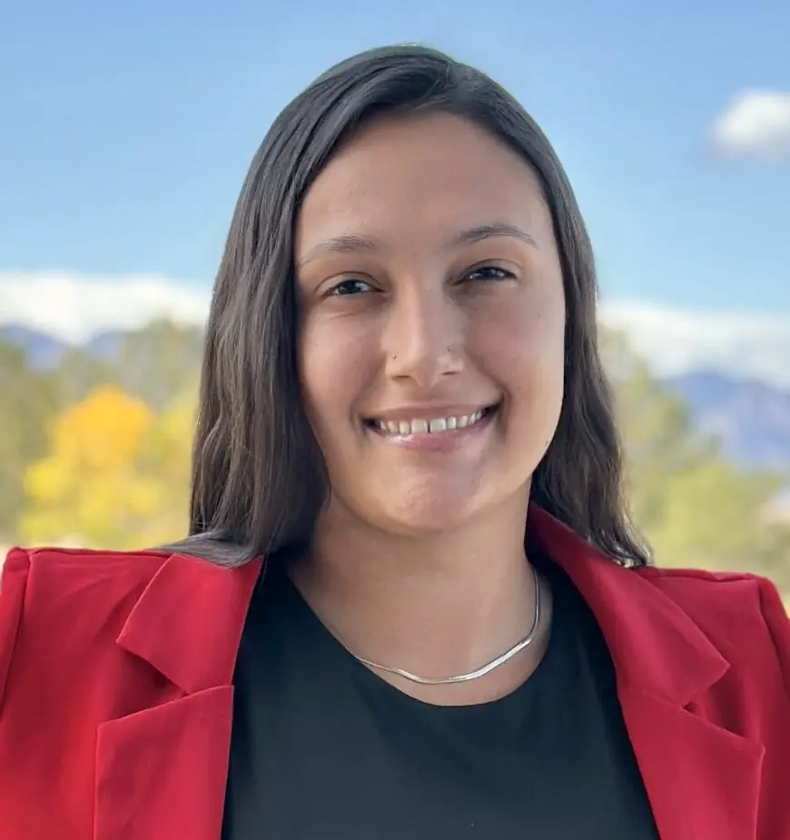 Woman wearing a black shirt and pink blazer, smiling at the camera.